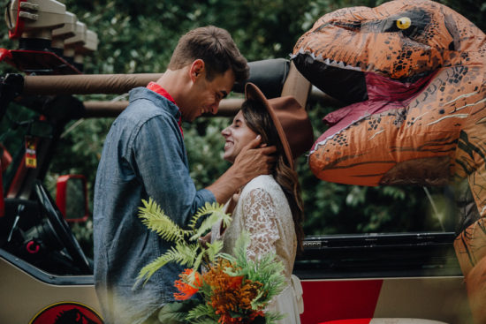 a bride and a groom look at each other by a trex and vehicle